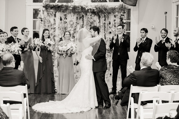 picture of a bride and groom first kiss at the wedding altar surrounded by friends and family cheering
