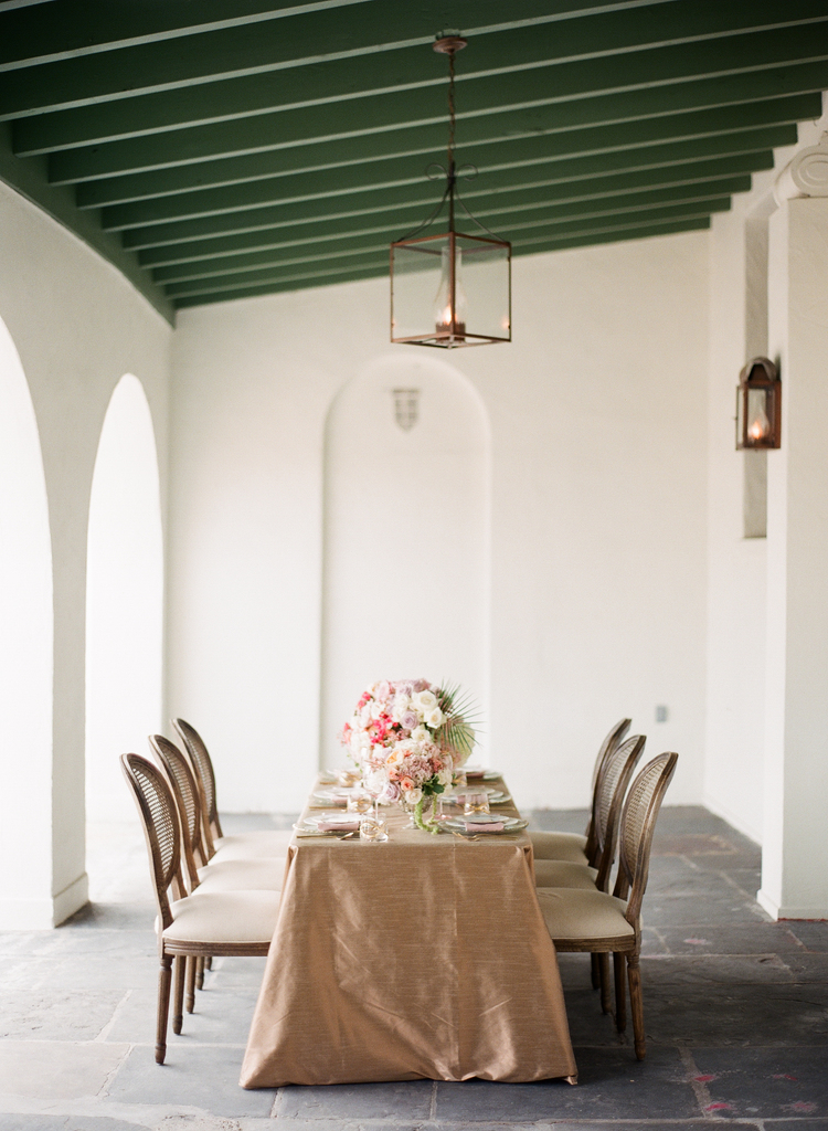 gold linens with a white pink and greenery floral arrangement and round back chairs
