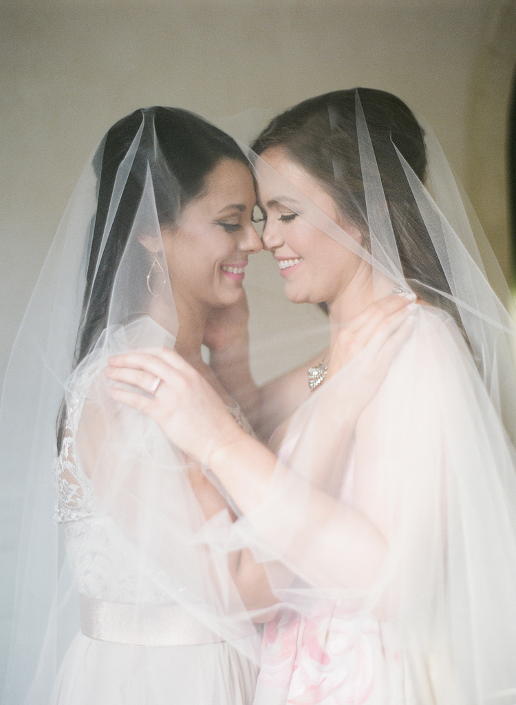 Brides under a white veil smile and hug