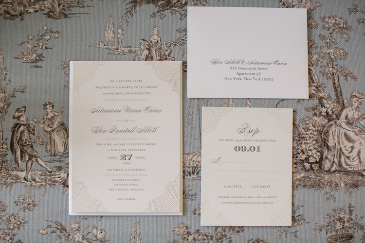 Classic white and black wedding invitations in cursive sitting on top of a toile pattern