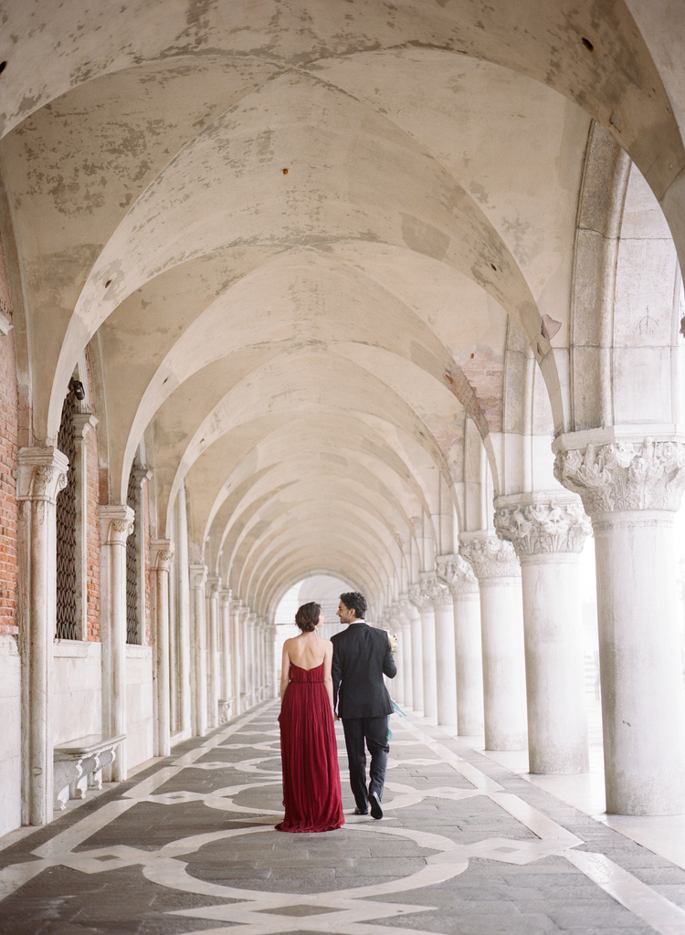 Bride and groom walking under an archway with tall pillars in Venice, italy