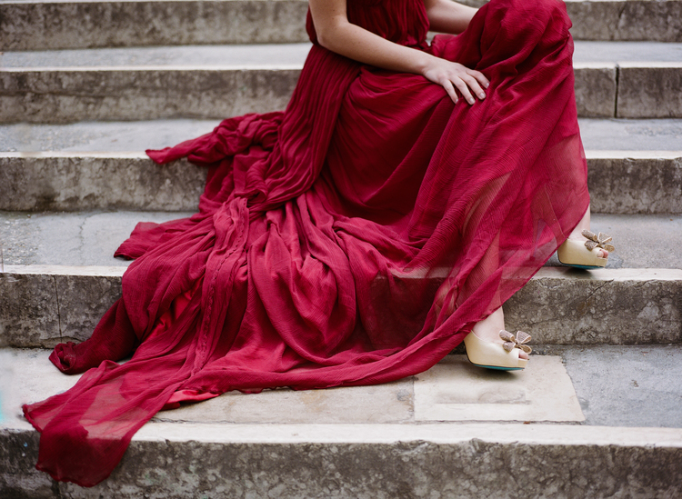 Bride sitting on steps letting her red dress flow down the stairs 