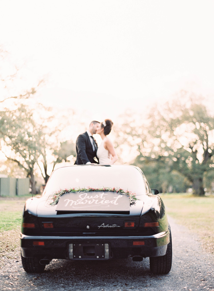 Bride and groom kiss out of the sunroof of the getaway car