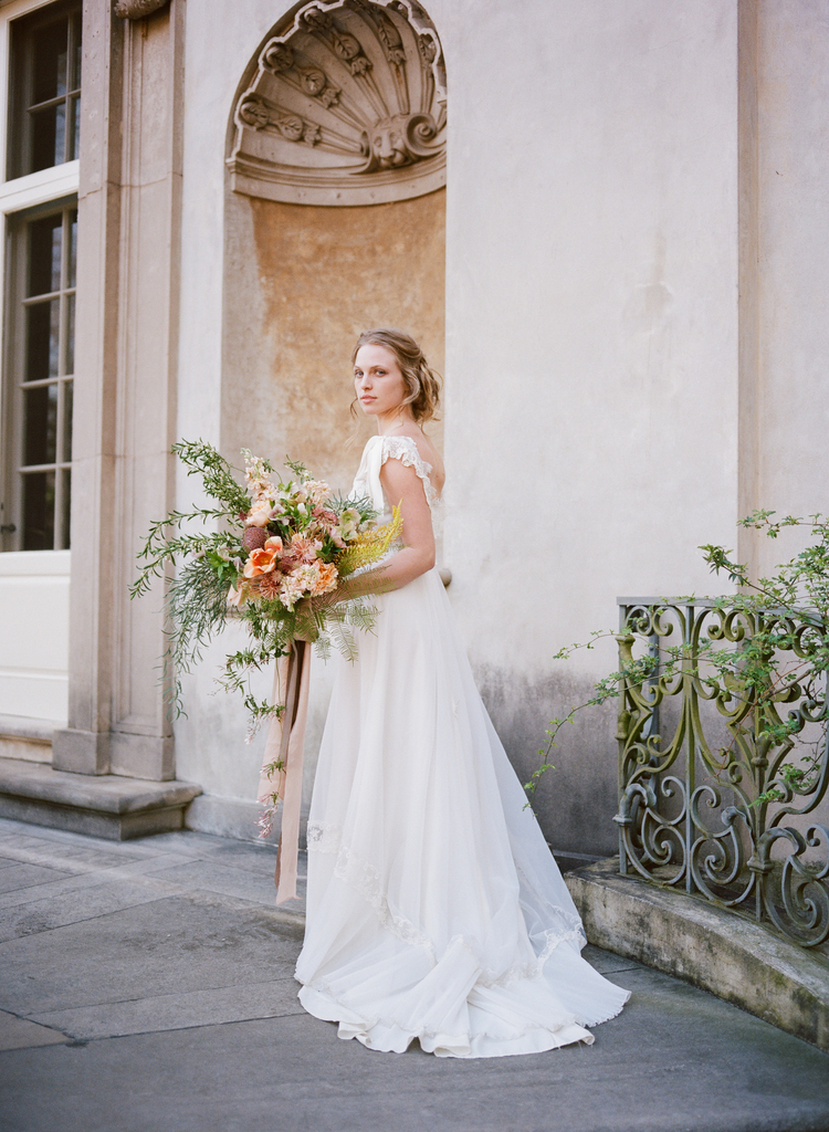 a bride stands in front of a fountain with her long white wedding gown and lush organic bouquet of flowers 
