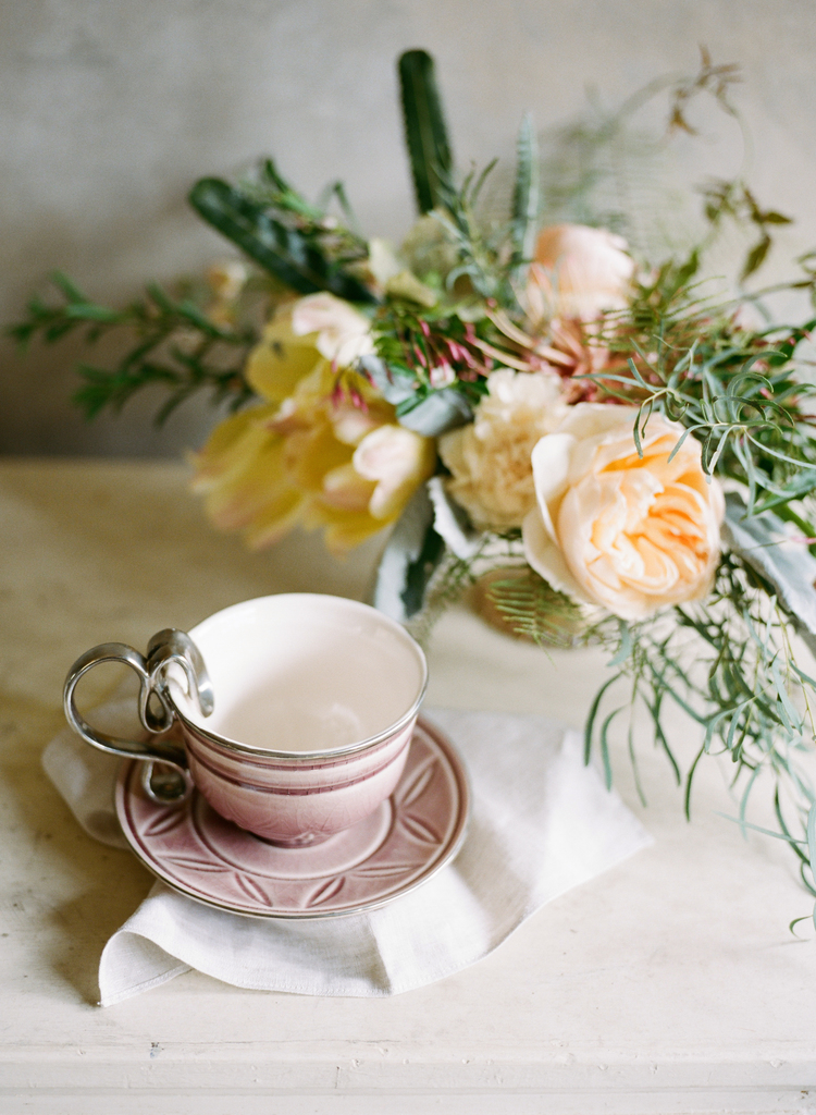Blush pink teacup next to light peach flowers and greenery on a table