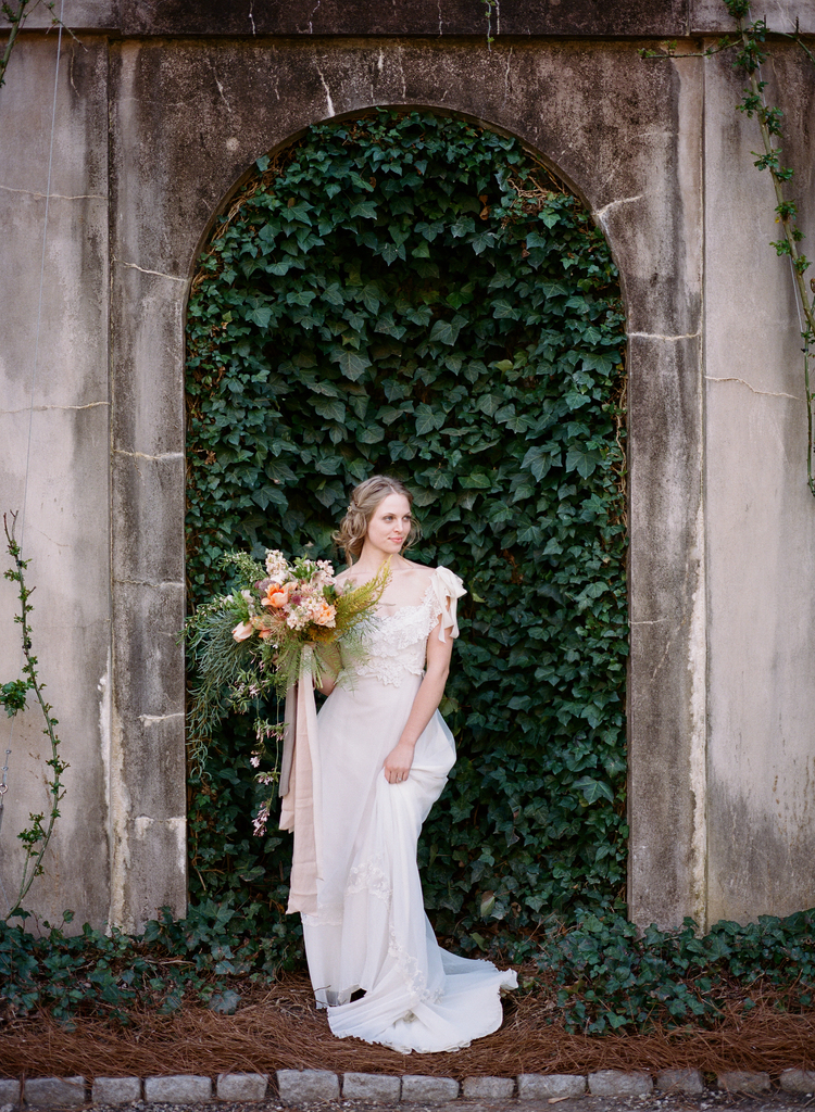 Bride posing in front of an arch of ivy holding her bouquet in her white wedding gown 