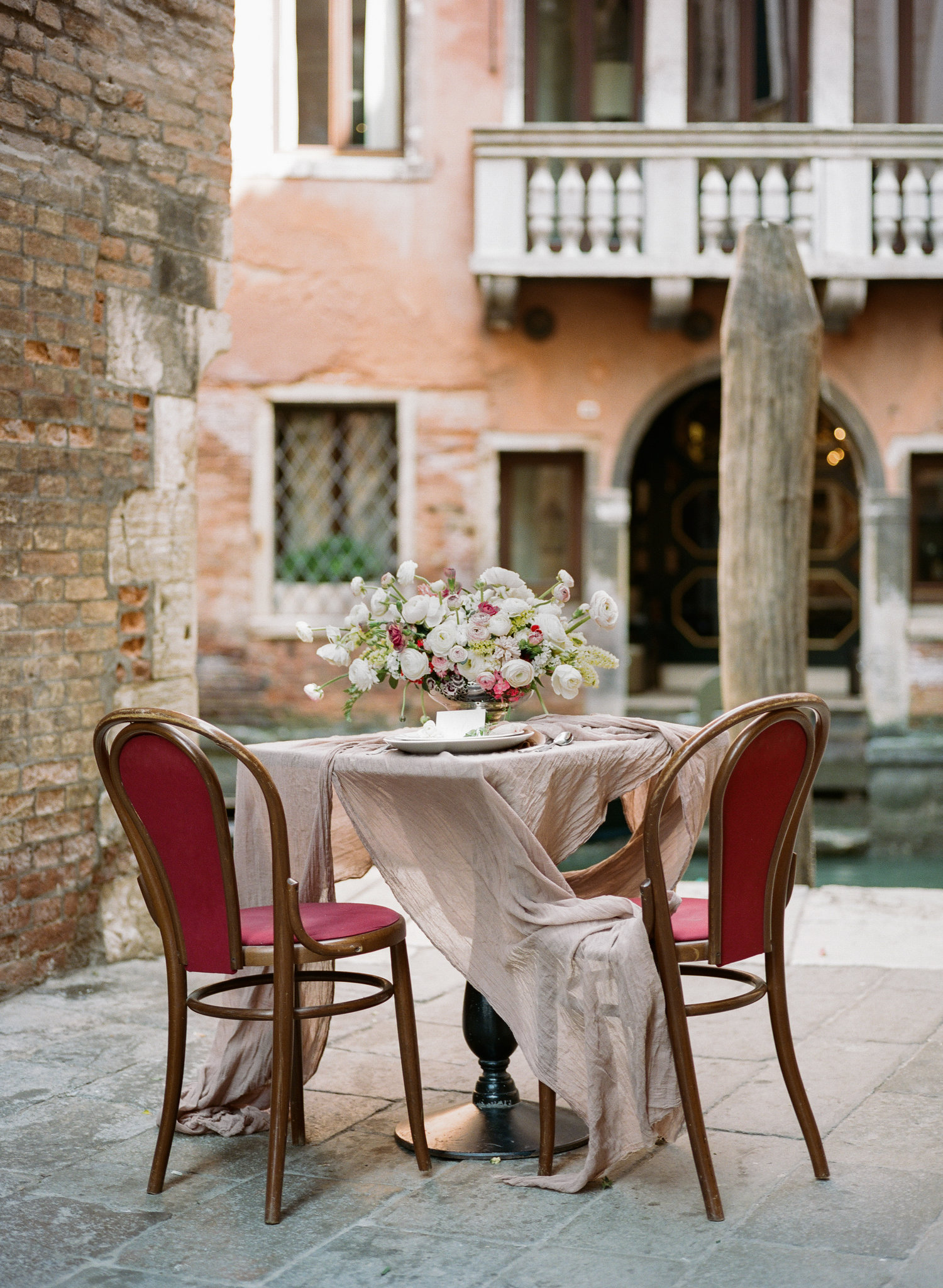 table for two with red chairs and pink and white florals by the canal in Venice Italy 