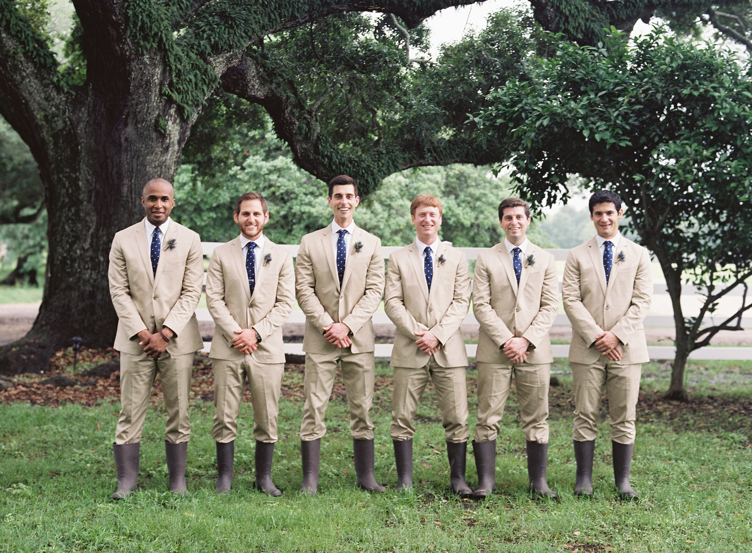 Groomsmen smile for the camera in their khaki suits and dark brown rain boots ready for the wedding at Stella Plantation 
