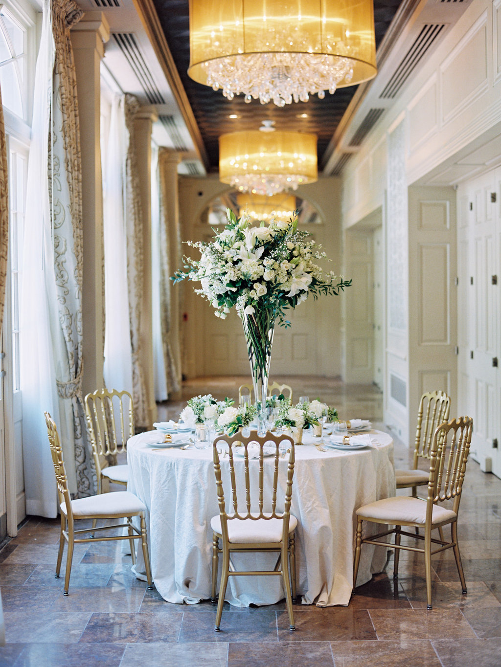 Tall white and green floral arrangement in the middle of a round table with a white table linen set for the wedding reception 