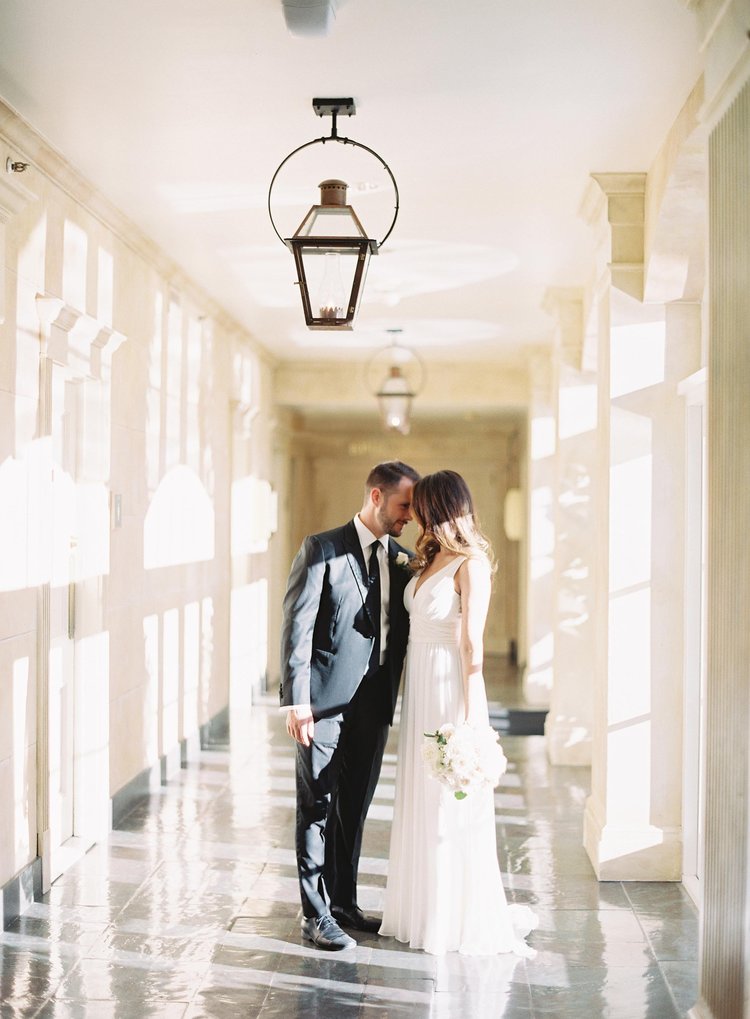 bride and groom embracing while standing in a long hallway with window light