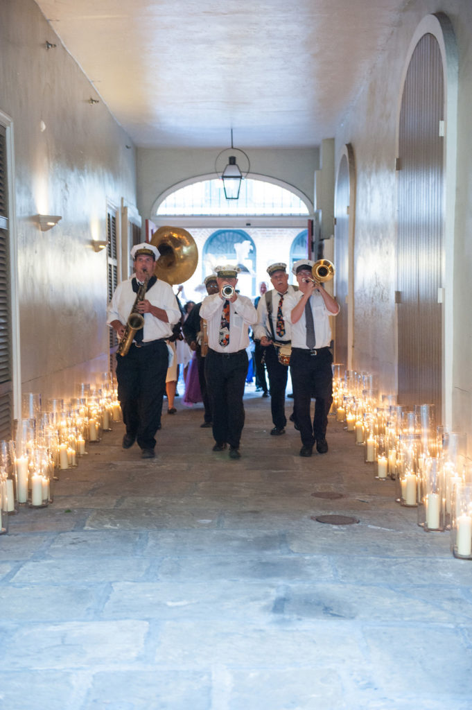 New Orleans Brass Band walking into courtyard through carriageway entrance lit by pillar candles in glass vases