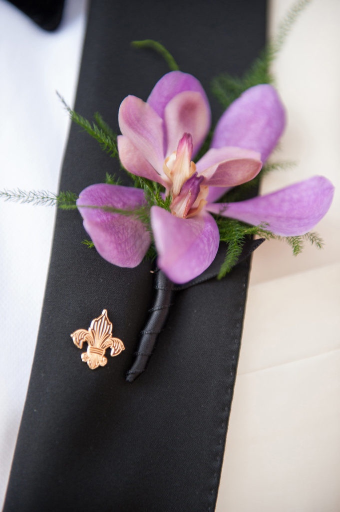 closeup of groom's black lapel with fleur de lis lapel pin and purple orchid boutonniere
